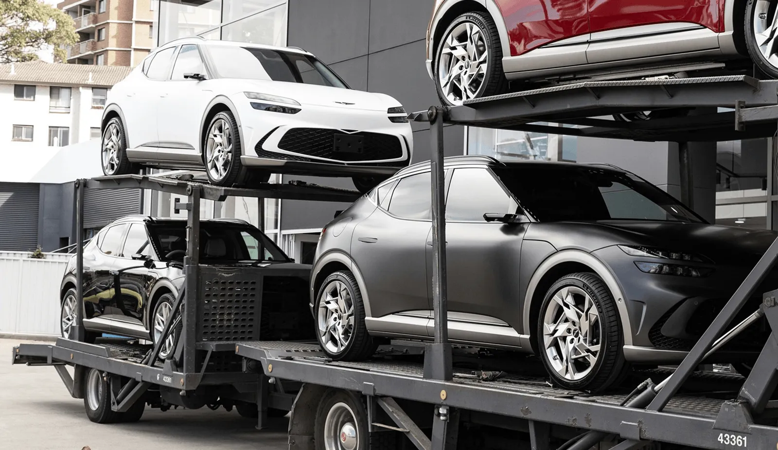 Two-tier auto carrier loaded with SUVs and sedans parked at a dealership lot ready for unloading, representing the dealership, auction, and fleet vehicle moves Curri runs with local drivers nationwide.