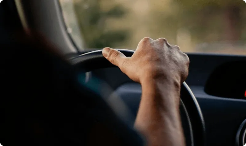 Driver's hand grips the steering wheel of a cargo van on an auto parts final-mile run, delivering filters, gaskets, and tires from a distributor's DC to the mechanic's bay on Curri's dispatch.